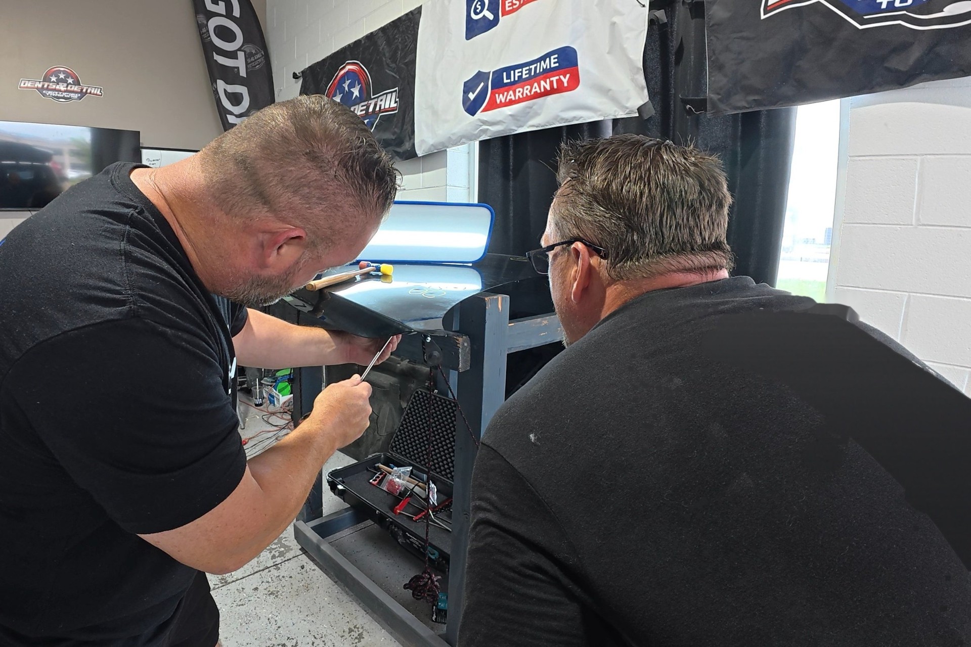 Dent College instructor teaching a student paintless dent repair on a black panel