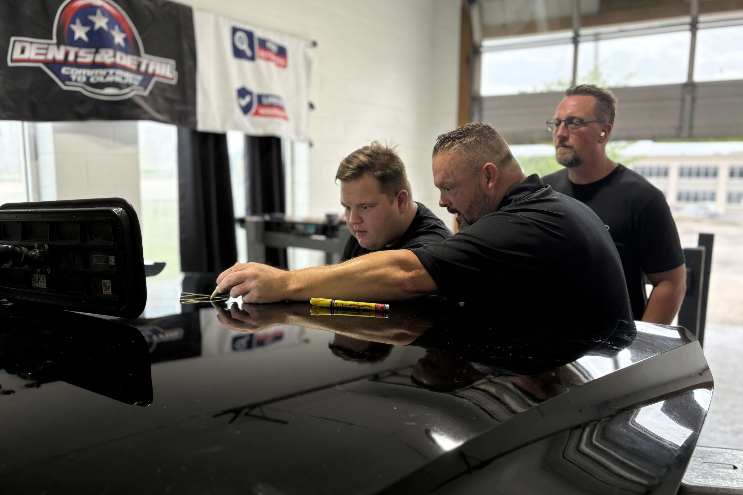 Dent College instructor teaching a student paintless dent repair on a black panel